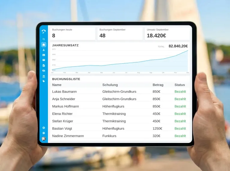 Tablet mit deutschsprachigem Butlerapp-Dashboard für Flugschulkurse und Zahlungen vor einem unscharfen Yachthafen