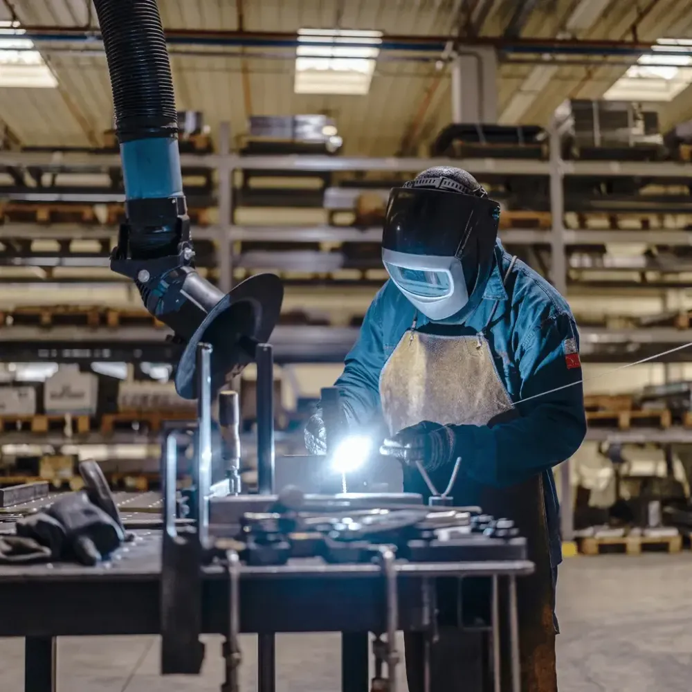 Schweißer in Schutzkleidung arbeitet in einer Werkstatt an einem Metallbauteil
