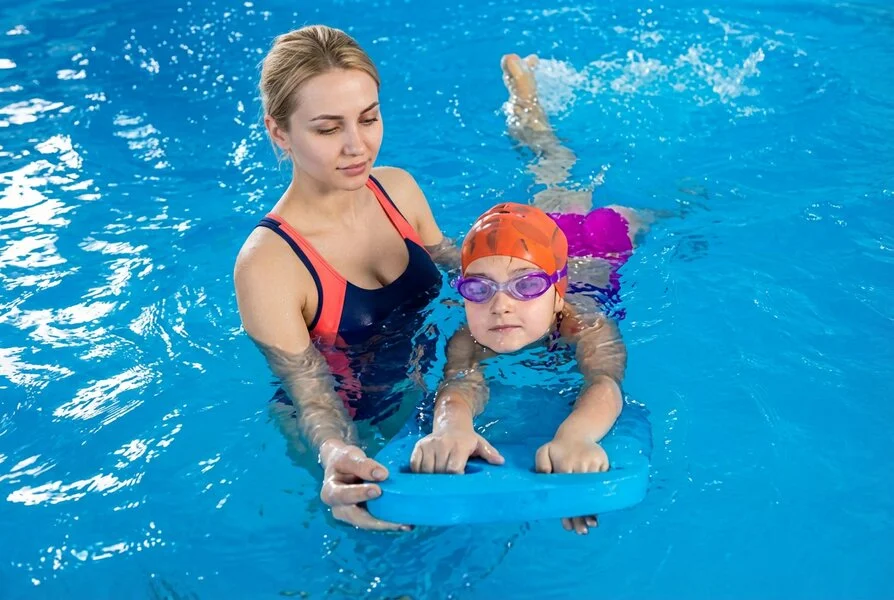 Kind lernt schwimmen im Hallenbad mit Schwimmbrett und Schwimmlehrer
