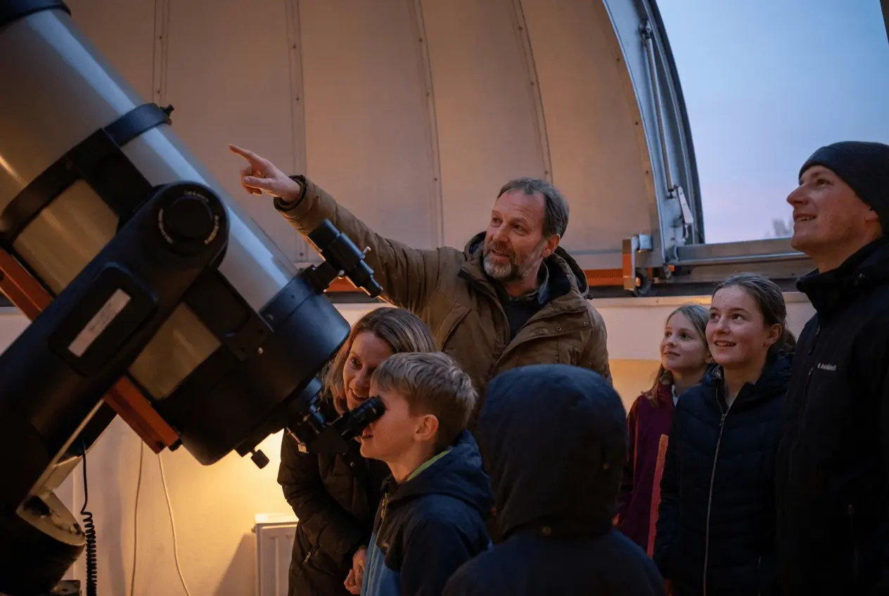 Besucher in einer Sternwarte schauen durch ein großes Teleskop in den Sternenhimmel bei einer öffentlichen Führung